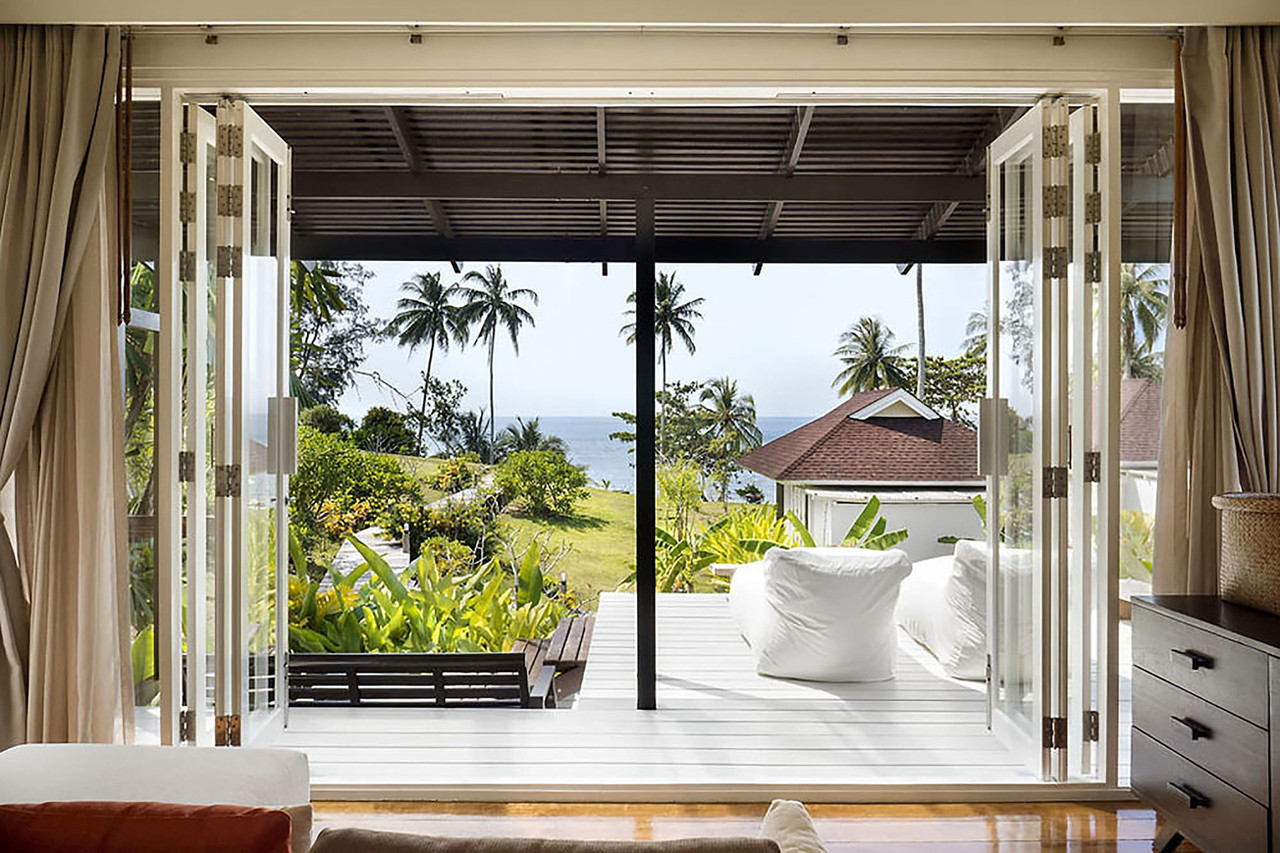 Villa with folding glass walls open to a timber deck, garden and sea views at Shantaa Koh Kood