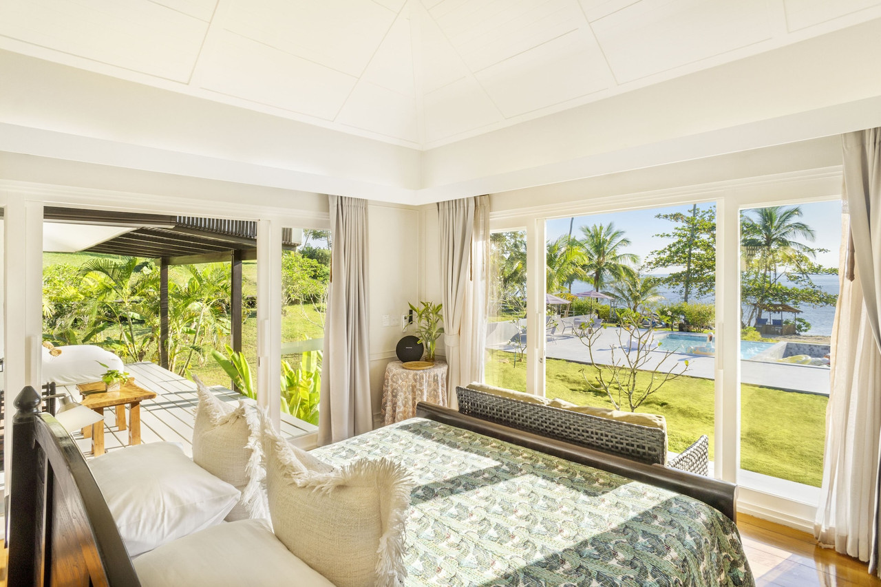 Villa bedroom looking out to the pool and sea through tall windows