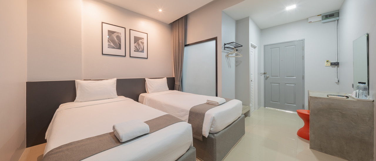 ห้องพักเตียงคู่สไตล์ Loft ของ C2U Hotel Uthai Thani หัวเตียงเทา โต๊ะปูนเปลือย พื้นกระเบื้องขาว