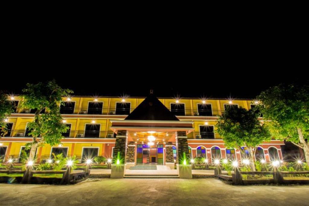 ตัวตึก Maladee Hotel ยามค่ำ อาคารสีเหลืองเปิดไฟ มีโถงทางเข้าหลังคาทรงจั่วและไฟส่องสว่างรอบสวนหน้าตึก