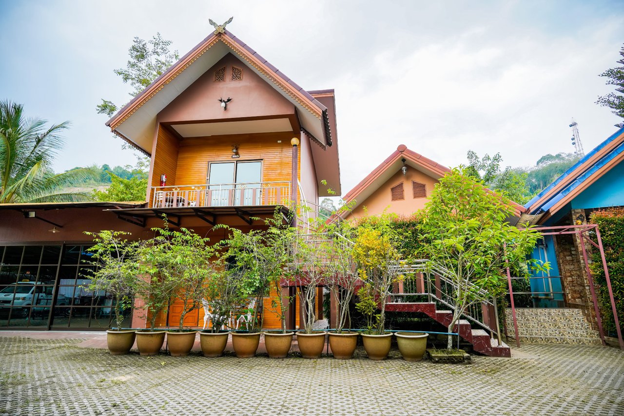 บ้านไม้สไตล์ชาเลต์ของ Happy Garden Resort Betong กลางวัน มีต้นไม้และกระถางในลานหิน